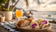 A wooden table holds a round wooden platter with freshly baked bread and open-faced sandwiches garnished with vibrant purple flowers, thin lemon slices, and fresh greens. A glass of orange juice glows beside a silver fork on a checkered cloth. In the background, blurred palm trees and a serene beach enhance the tropical ambiance under soft sunlight. Ai generated. Photography style.