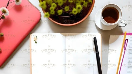 An open notebook with blank pages lies at the center, accompanied by a black pen resting on its cover. To the left, a coral-colored laptop sleeve contrasts with the white desk. A potted plant with delicate green flowers adds a natural touch. A cup of tea sits on a white saucer at the top right. A document with colorful paper clips and a yellow pencil is positioned nearby, creating a balanced composition with soft lighting. Ai generated. Photography style.