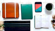 Flat lay image on a white surface featuring an orange case with white straps, a green notebook, and a colorful phone with a geometric design. An open planner with minimal lines lies nearby. A white cup with green powder, wooden containers, and a stack of dark blue organizers are arranged neatly. A wooden tray with green leaves adds a natural touch. The composition is clean and modern with balanced elements. Ai generated. Photography style.