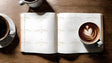 Flat lay image on a wooden surface featuring an open blank notebook with cream-colored pages. On the right page, a white cup of coffee with latte art in the shape of a heart is placed. To the left, another white cup of black coffee sits on a saucer. A third cup is partially visible at the top. The rich brown tones of the coffee contrast with the light notebook pages. The arrangement is clean and minimal. Ai generated. Photography style.