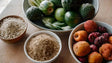 This image shows four bowls filled with natural ingredients. One bowl contains puffed grains, another has fine powdered grains. A third bowl holds green vegetables, including cucumbers and zucchini, while the last bowl is filled with wrinkled fruits in shades of orange and red. The scene is set on a light wooden surface, emphasizing the fresh and wholesome look of the items. Ai generated. Photography style.