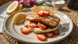 A plate of grilled chicken with visible grill marks sits on soft flatbread, topped with slices of fresh cherry tomatoes. A lemon wedge is placed on the side for added flavor. The background shows soft pink flowers and simple tableware, creating a warm and inviting feel. The meal looks fresh and colorful, served on a plain plate with a woven mat underneath for a natural touch. Ai generated. Photography style.