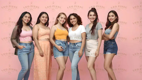 Six women pose in front of a pink background, wearing casual summer outfits. They sport bright tops in striped, yellow, white, and blue, paired with denim shorts, jeans, and a flowy peach dress. Their hair is styled in various ways, from loose waves to a high ponytail. Each woman exudes confidence and warmth, standing together in a friendly and relaxed formation. Ai generated. Photography style.