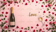 A soft pink background features a champagne bottle with a gold neck and blank label, a tilted wine glass with golden liquid, and a glittering "Love" centerpiece. Red hearts, scattered rose petals, vibrant pink roses with green leaves, and delicate heart-shaped accents frame the scene. The composition creates a visually appealing and romantic aesthetic. Ai generated. Flat lay photography style.