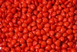 A close-up shot of glossy red heart-shaped candies fills the entire frame. The candies are packed tightly together, creating a textured surface with soft highlights reflecting off their smooth coating. The vibrant red color stands out, making the image bright and eye-catching. The focus is sharp, capturing each detail, while the lighting enhances the glossy look, giving a warm and inviting feel. Photography.