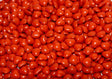 A close-up shot of glossy red heart-shaped candies fills the entire frame. The candies are packed tightly together, creating a textured surface with soft highlights reflecting off their smooth coating. The vibrant red color stands out, making the image bright and eye-catching. The focus is sharp, capturing each detail, while the lighting enhances the glossy look, giving a warm and inviting feel. Photography.