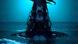 A figure sits knee-deep in water, wearing a dark dress and a pointed hat. The long, flowing hair blends with the rippling waves around them. The water reflects soft, glowing highlights under a serene blue light. The background is a gradient of darker blues, evoking depth and calm. The figure’s shadowed features and delicate details enhance the image’s mysterious tone. Ai generated. Anime style.