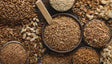 This image shows a collection of seeds in different bowls and spread across a wooden surface. The seeds include sunflower seeds, pumpkin seeds, and others in shades of brown and cream. A wooden scoop rests in one bowl, adding detail to the arrangement. The textures of the seeds and bowls are clear, creating a natural and earthy look. Ai generated. Photography style.