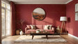 A cozy living room with a deep red wall serves as the backdrop for a light pink sofa adorned with cream and pink pillows. A circular wall art piece depicting a serene landscape is the focal point. A soft rug underlines a wooden coffee table. To the left, long curtains frame a glass door. Elegant vases and a sleek floor lamp add charm to this warm, inviting space. Ai generated. Photography style.